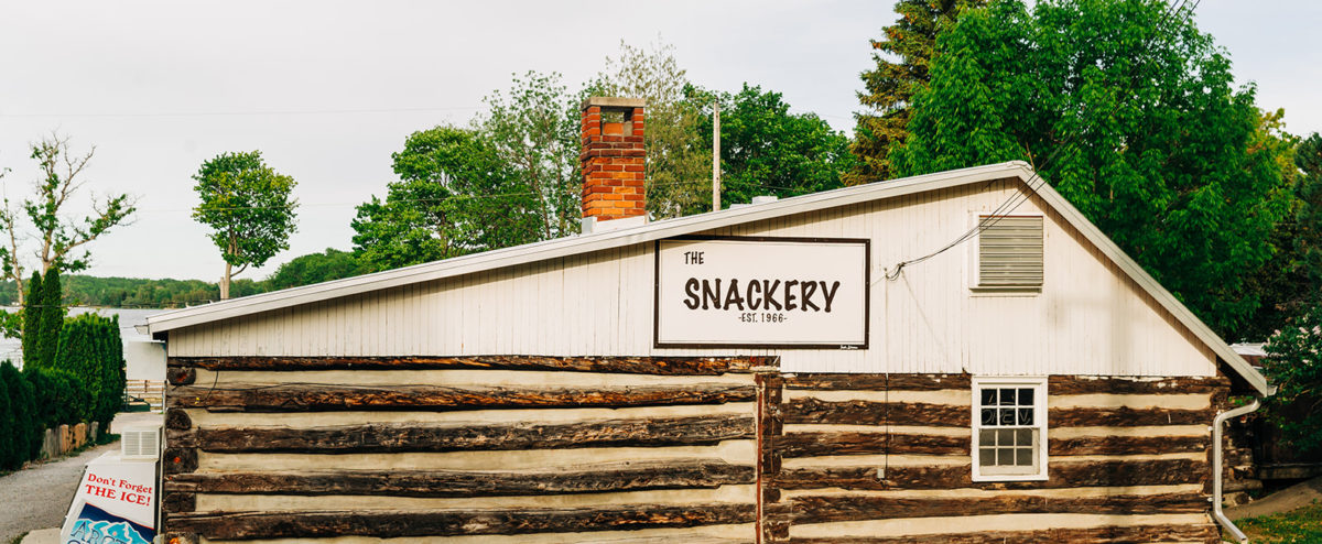 The snackery, a large and rustic log building with a brick chimney as viewed from Elim Lodge Road
