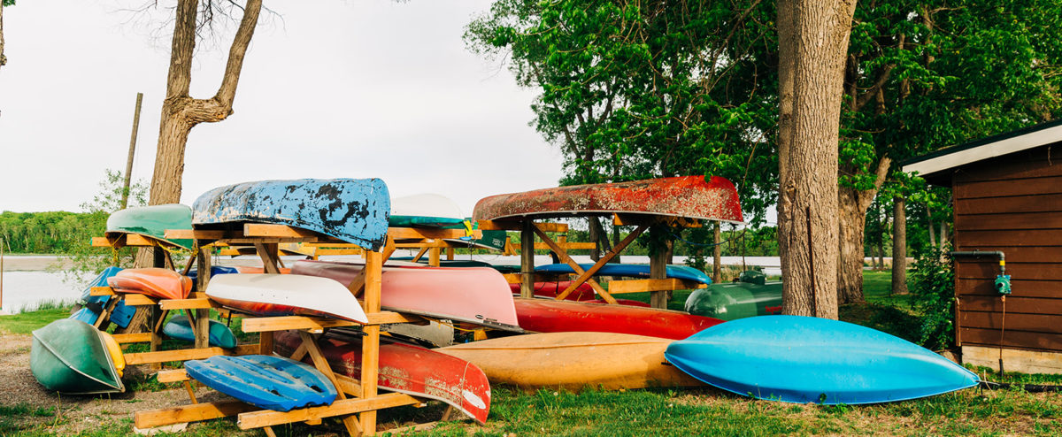 Canoes sit on a rack in front of Pigeon Lake at Elim Lodge, available for rental