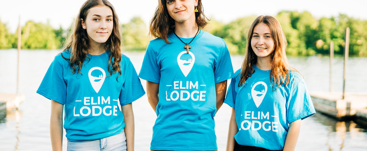 Three youth stand at the Lakeside wearing blue Elim Lodge T-shirts